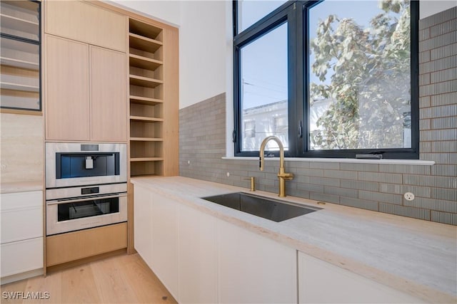 kitchen featuring stainless steel double oven, sink, light hardwood / wood-style flooring, and backsplash