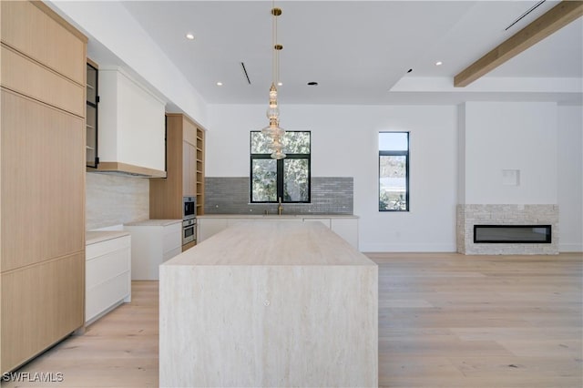 kitchen with tasteful backsplash, decorative light fixtures, a center island, light brown cabinets, and white cabinets