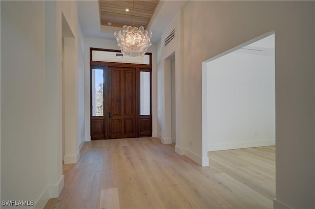 foyer with a tray ceiling, light hardwood / wood-style floors, and a chandelier