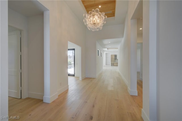 corridor featuring a towering ceiling, light hardwood / wood-style floors, and a chandelier