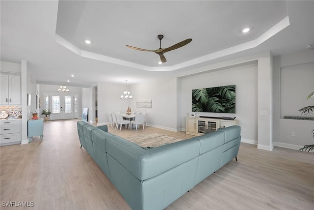 living room featuring french doors, ceiling fan with notable chandelier, light hardwood / wood-style flooring, and a raised ceiling