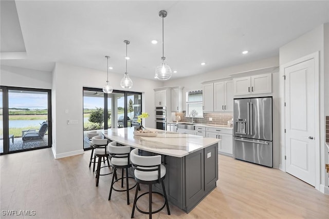 kitchen with pendant lighting, white cabinets, light hardwood / wood-style floors, appliances with stainless steel finishes, and a kitchen island