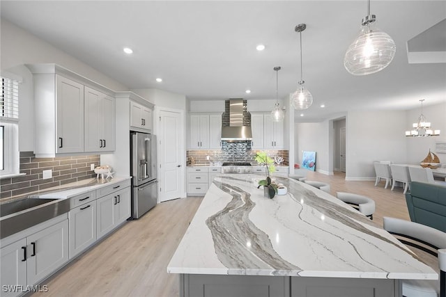 kitchen featuring a spacious island, pendant lighting, stainless steel appliances, and wall chimney range hood