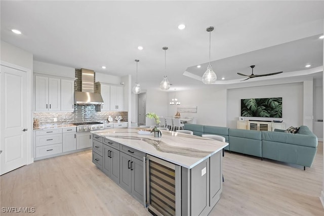 kitchen with white cabinetry, beverage cooler, wall chimney range hood, decorative light fixtures, and a kitchen island with sink