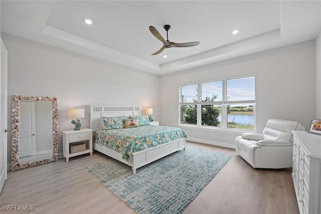 bedroom with a tray ceiling, ceiling fan, hardwood / wood-style floors, and a water view