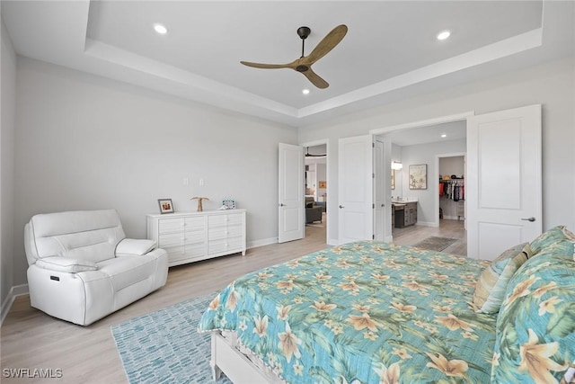 bedroom featuring a raised ceiling, ceiling fan, light hardwood / wood-style flooring, and ensuite bathroom