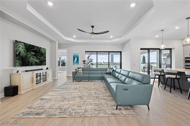 living room with ceiling fan, light wood-type flooring, and a tray ceiling