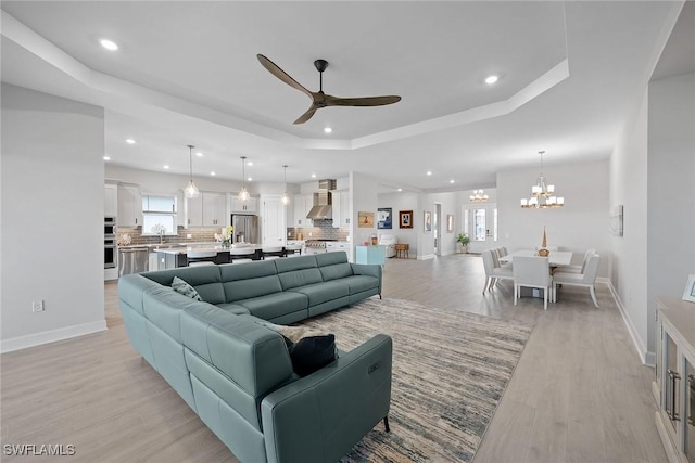 living room featuring a tray ceiling, light hardwood / wood-style flooring, ceiling fan with notable chandelier, and sink