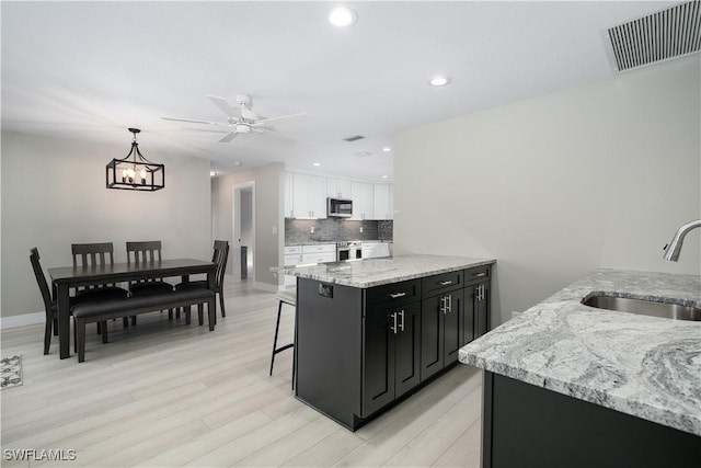 kitchen with ceiling fan with notable chandelier, sink, light hardwood / wood-style floors, white cabinetry, and hanging light fixtures