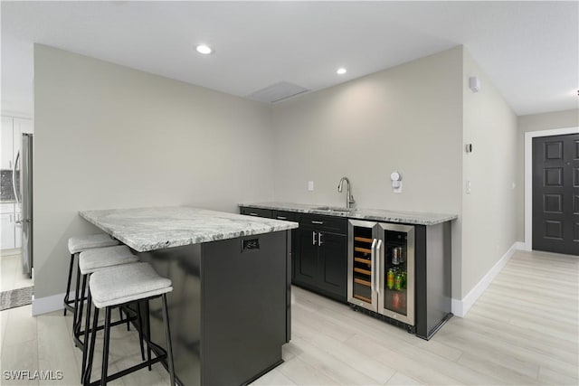 kitchen with light wood-type flooring, light stone counters, a breakfast bar, beverage cooler, and stainless steel refrigerator