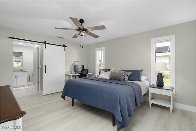 bedroom featuring ceiling fan, a barn door, ensuite bathroom, and multiple windows