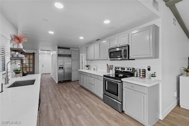 kitchen with light wood-type flooring, appliances with stainless steel finishes, sink, and gray cabinetry