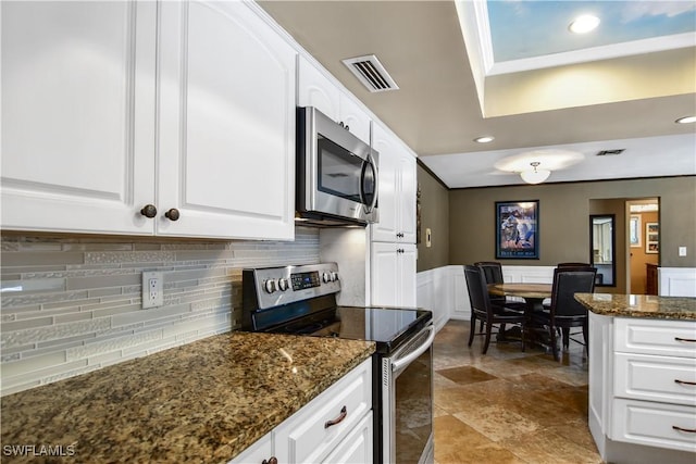 kitchen featuring tasteful backsplash, white cabinetry, dark stone counters, and appliances with stainless steel finishes