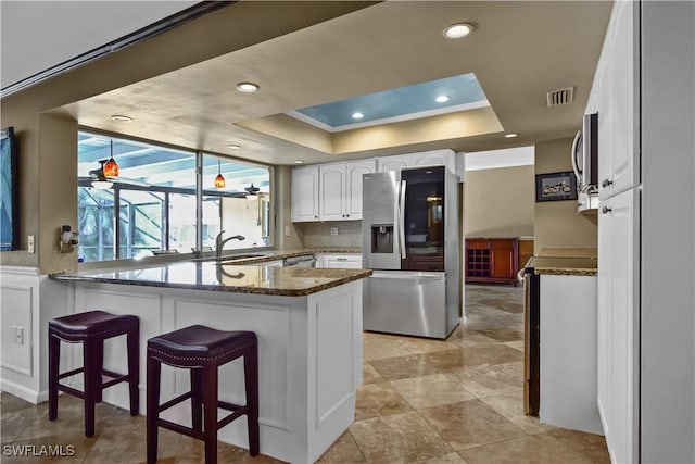 kitchen with dark stone countertops, kitchen peninsula, white cabinets, and stainless steel appliances