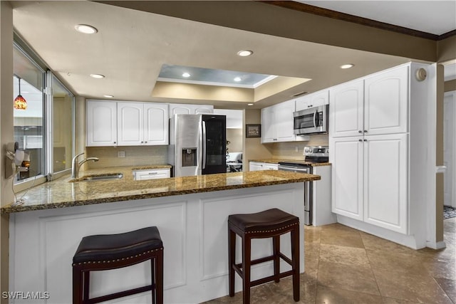 kitchen with kitchen peninsula, appliances with stainless steel finishes, sink, dark stone countertops, and white cabinets