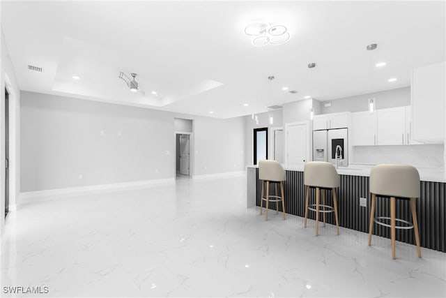 kitchen with a breakfast bar, a raised ceiling, hanging light fixtures, white cabinets, and white fridge with ice dispenser