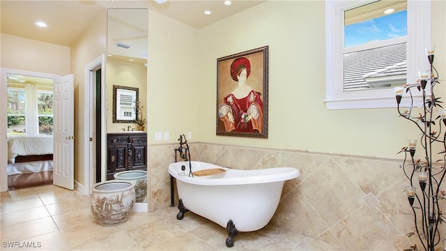 bathroom with a tub to relax in, plenty of natural light, vanity, and tile walls