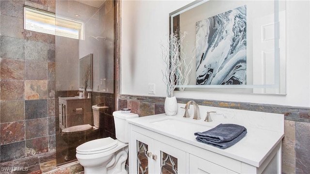 bathroom with tiled shower, vanity, toilet, and tile walls