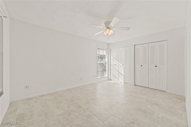 unfurnished bedroom featuring ceiling fan, light tile patterned floors, and two closets