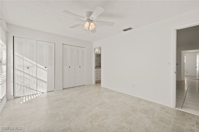 unfurnished bedroom with light tile patterned floors, connected bathroom, ceiling fan, and multiple closets