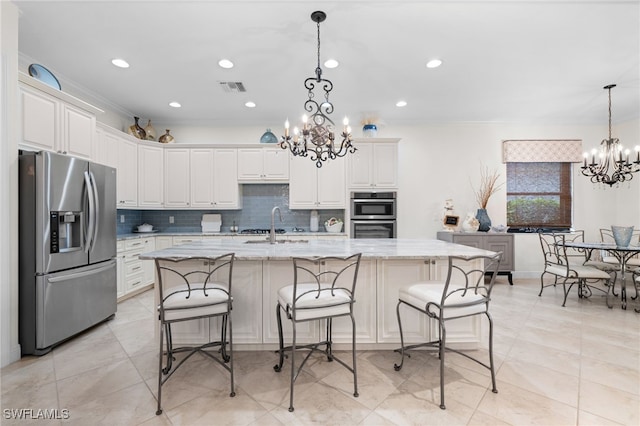 kitchen featuring light stone countertops, hanging light fixtures, a notable chandelier, a center island with sink, and appliances with stainless steel finishes