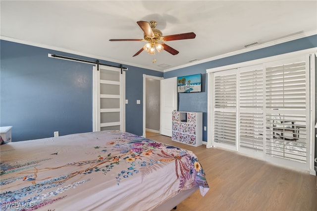 bedroom with a barn door, ceiling fan, crown molding, and light hardwood / wood-style floors