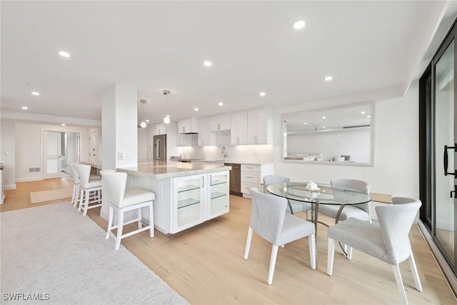 kitchen with light stone countertops, sink, decorative light fixtures, white cabinets, and light hardwood / wood-style floors