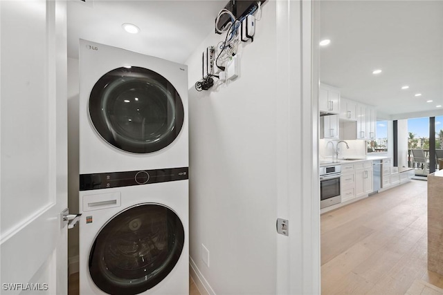 clothes washing area with stacked washer / drying machine, light hardwood / wood-style floors, and sink