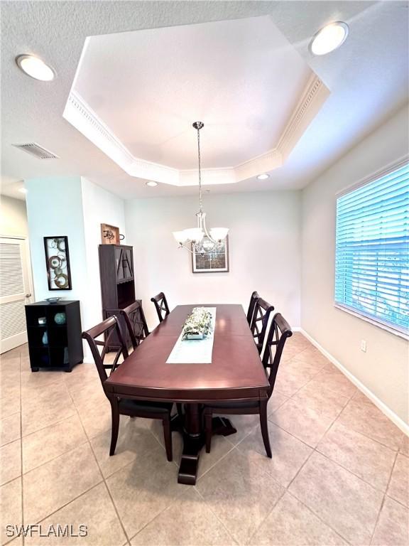 tiled dining room featuring a chandelier, a raised ceiling, and ornamental molding