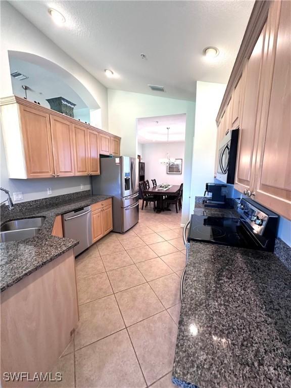 kitchen featuring dark stone counters, stainless steel appliances, sink, light brown cabinets, and light tile patterned flooring