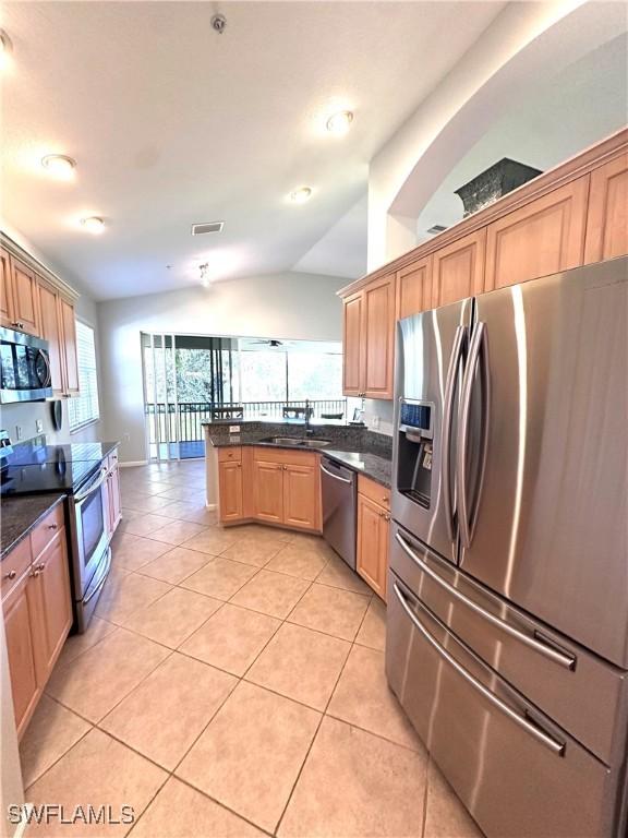 kitchen with dark stone counters, sink, vaulted ceiling, light tile patterned flooring, and stainless steel appliances