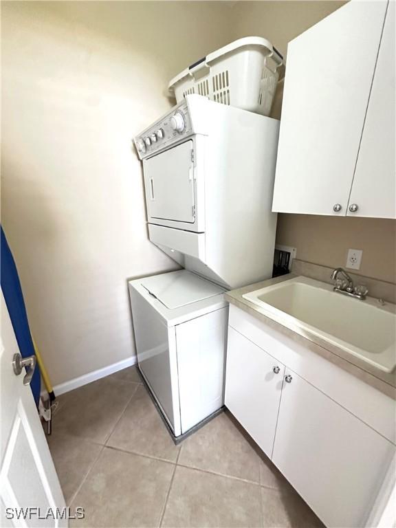 laundry room with cabinets, sink, light tile patterned floors, and stacked washing maching and dryer