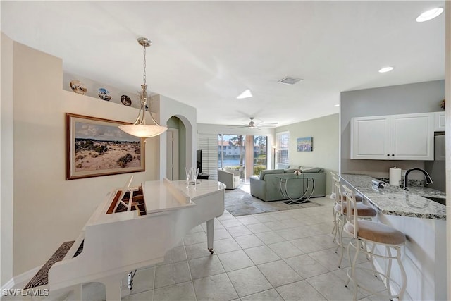 interior space featuring arched walkways, light tile patterned flooring, visible vents, baseboards, and a ceiling fan