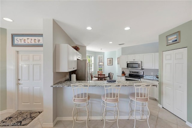 kitchen featuring stainless steel appliances, a breakfast bar, a peninsula, white cabinets, and light stone countertops