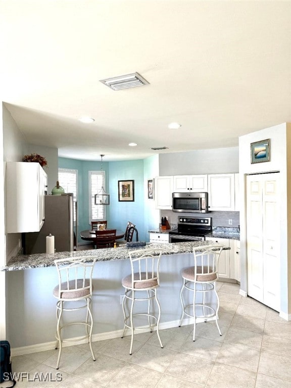 kitchen with white cabinets, a breakfast bar area, stainless steel appliances, and light stone counters