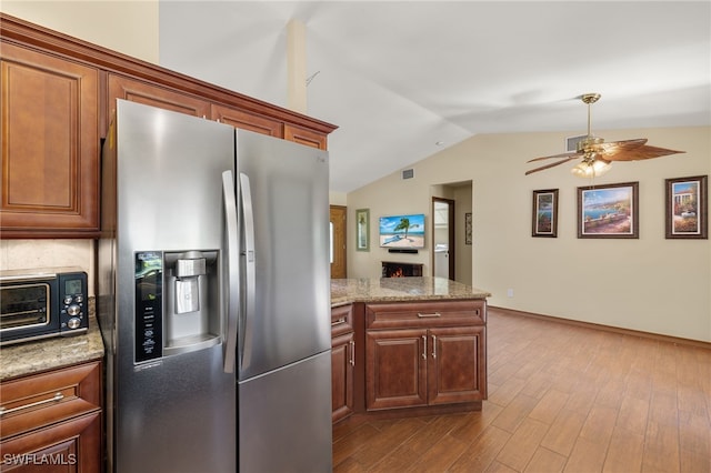 kitchen featuring vaulted ceiling, ceiling fan, stainless steel fridge, light stone countertops, and light hardwood / wood-style floors