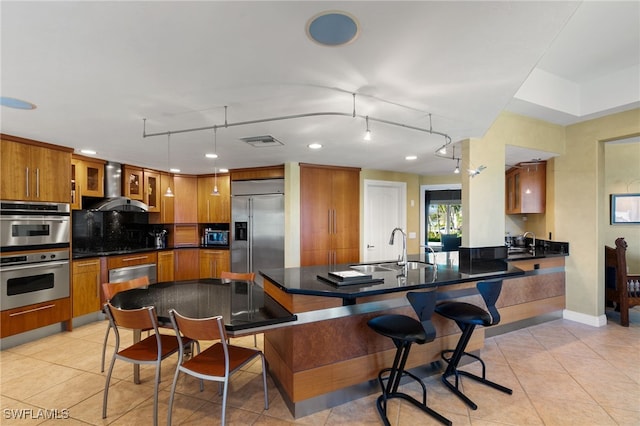 kitchen with a kitchen breakfast bar, sink, wall chimney exhaust hood, decorative light fixtures, and stainless steel appliances