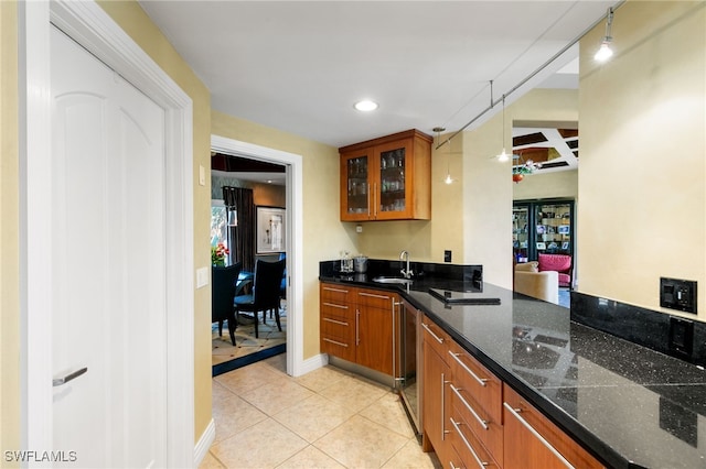 kitchen with kitchen peninsula, light tile patterned floors, sink, and dark stone counters