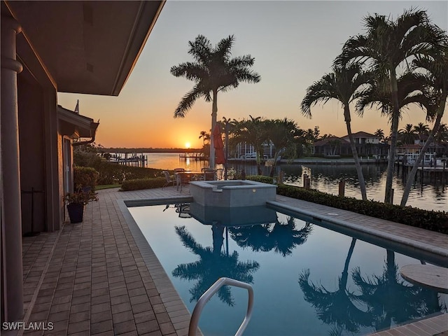 pool at dusk with an in ground hot tub, a water view, and a patio area