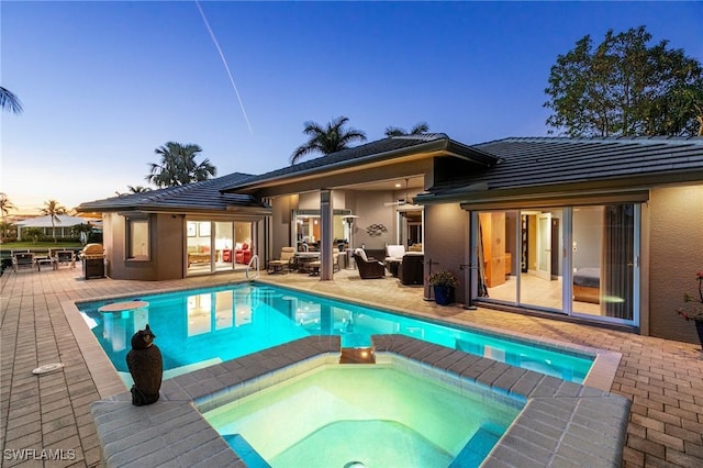 pool at dusk with an in ground hot tub and a patio area