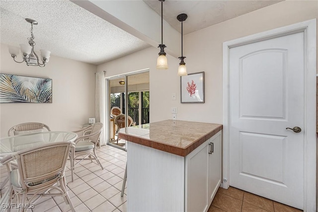 kitchen featuring a textured ceiling, pendant lighting, light tile patterned floors, a notable chandelier, and white cabinetry