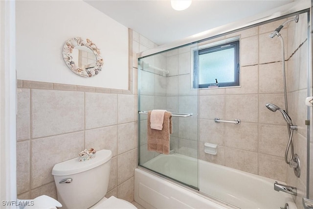 bathroom featuring toilet, tile walls, and bath / shower combo with glass door