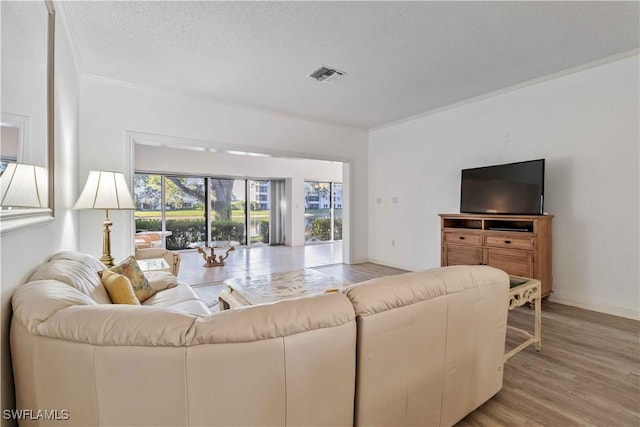 living room with light wood-type flooring, a textured ceiling, and ornamental molding