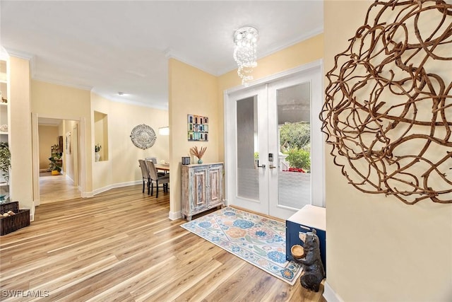 entrance foyer with a notable chandelier, light wood-type flooring, crown molding, and french doors