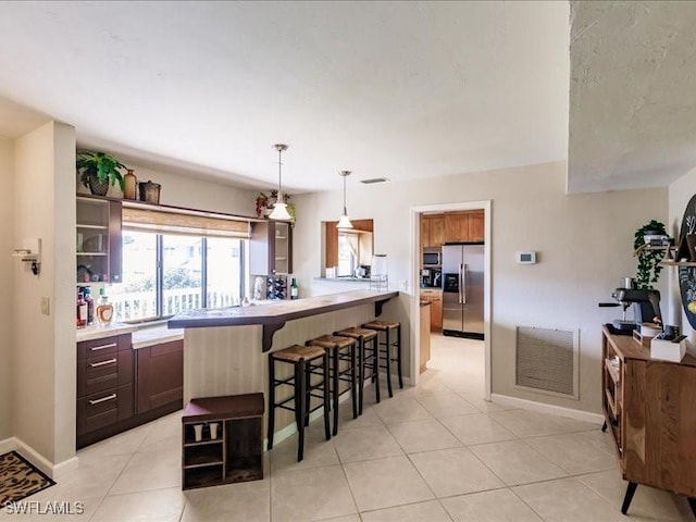 kitchen with a kitchen breakfast bar, hanging light fixtures, light tile patterned floors, dark brown cabinetry, and stainless steel appliances