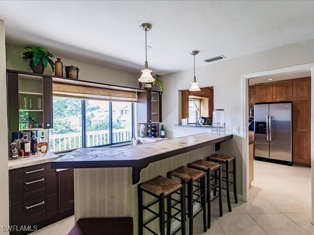 kitchen featuring a kitchen breakfast bar, stainless steel refrigerator with ice dispenser, decorative light fixtures, light tile patterned flooring, and kitchen peninsula