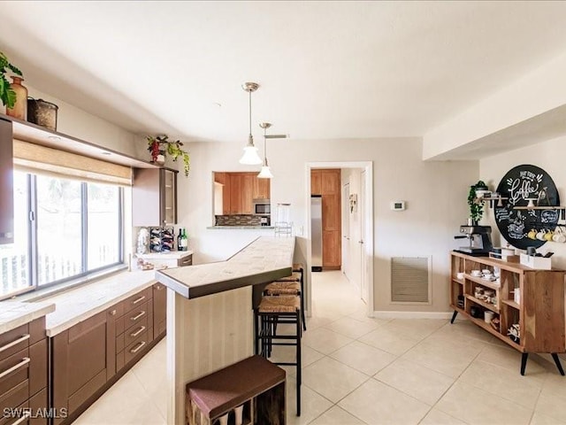 kitchen featuring hanging light fixtures, a kitchen island, appliances with stainless steel finishes, light tile patterned flooring, and a breakfast bar area