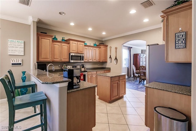 kitchen with dark stone countertops, kitchen peninsula, crown molding, and appliances with stainless steel finishes