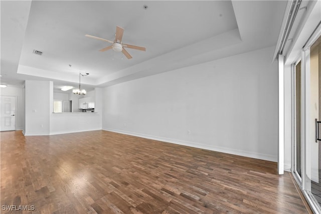 unfurnished living room with ceiling fan with notable chandelier, wood-type flooring, and a raised ceiling