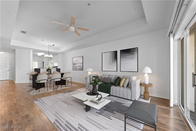 living room with hardwood / wood-style flooring, ceiling fan with notable chandelier, and a raised ceiling